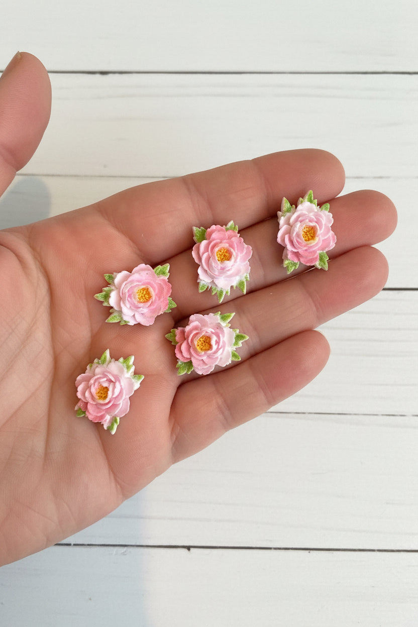 Small soft blue fabric flowers with green leaves held in a hand to show size, craft embellishments pack of 50