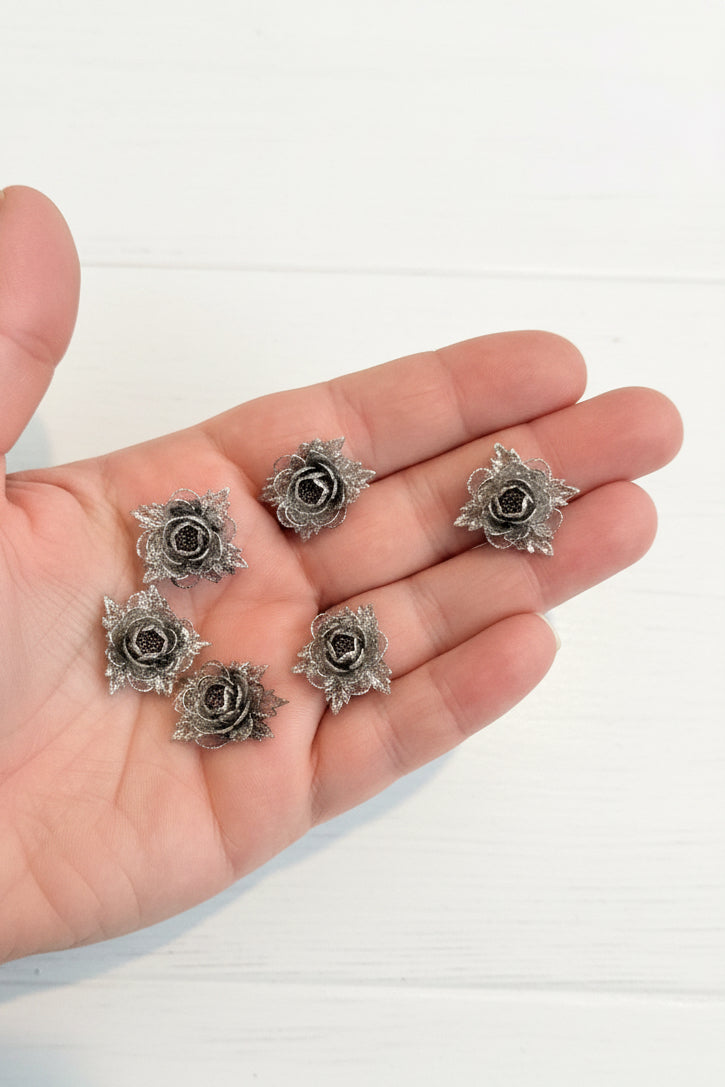 Small soft blue fabric flowers with green leaves held in a hand to show size, craft embellishments pack of 50