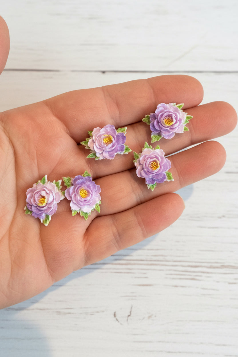 Small soft blue fabric flowers with green leaves held in a hand to show size, craft embellishments pack of 50