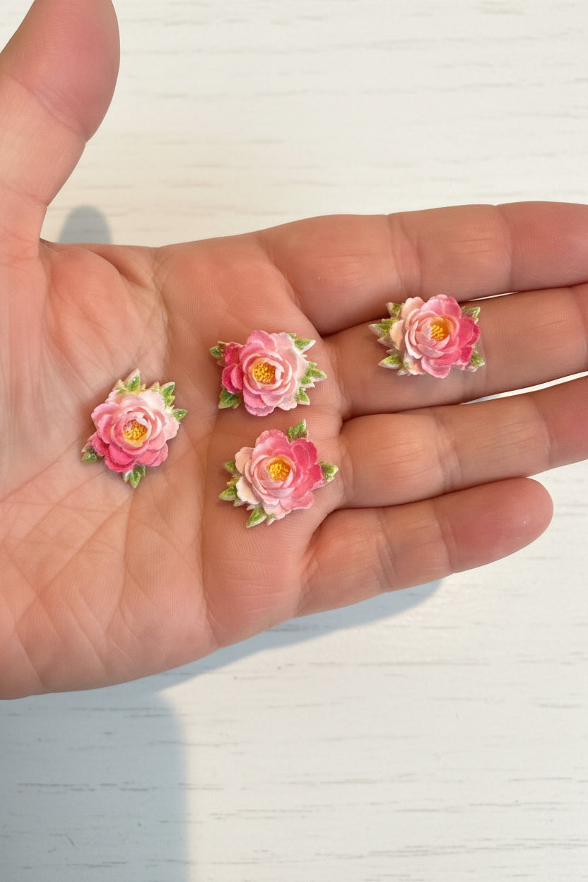 Small soft blue fabric flowers with green leaves held in a hand to show size, craft embellishments pack of 50