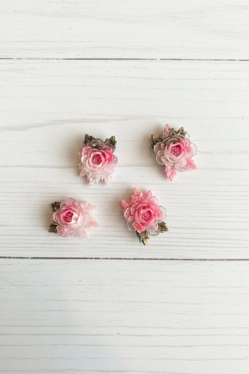 Small soft blue fabric flowers with green leaves held in a hand to show size, craft embellishments pack of 50