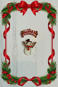 Acrylic Merry Christmas and snowman pendant set showing a colourful snowman charm with red scarf and top hat holding a Merry Christmas sign, on a white wood background with festive holly border