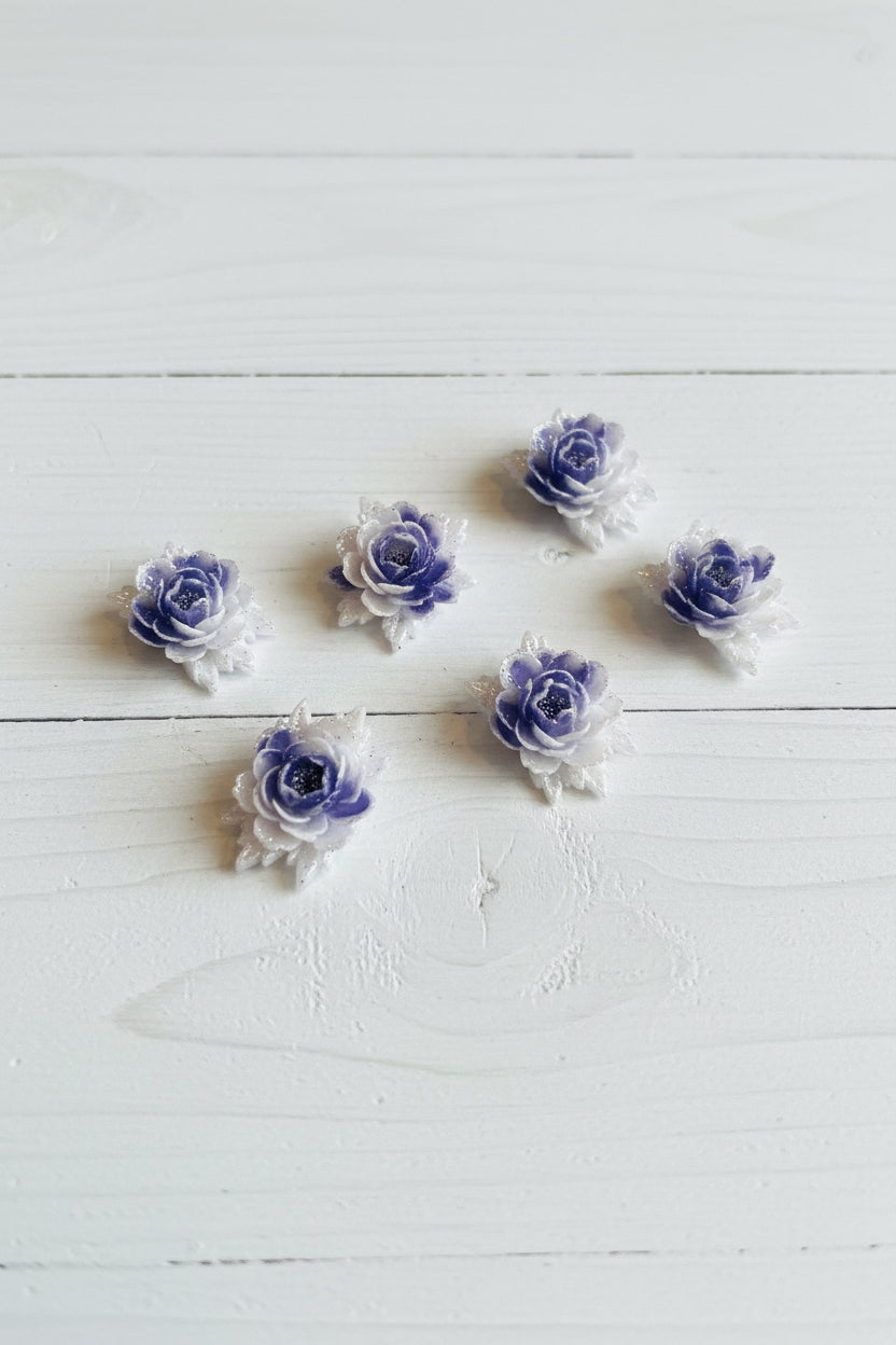 Small soft blue fabric flowers with green leaves held in a hand to show size, craft embellishments pack of 50