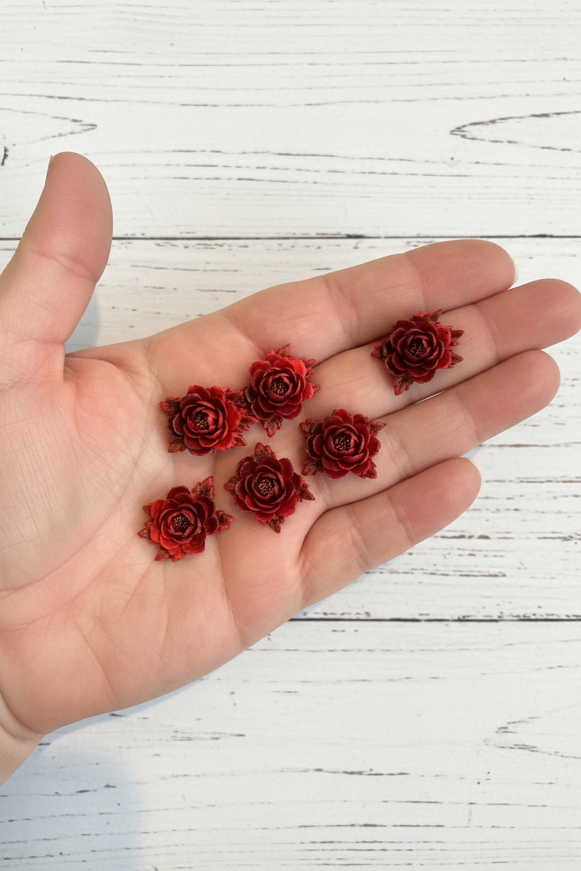 Small soft blue fabric flowers with green leaves held in a hand to show size, craft embellishments pack of 50