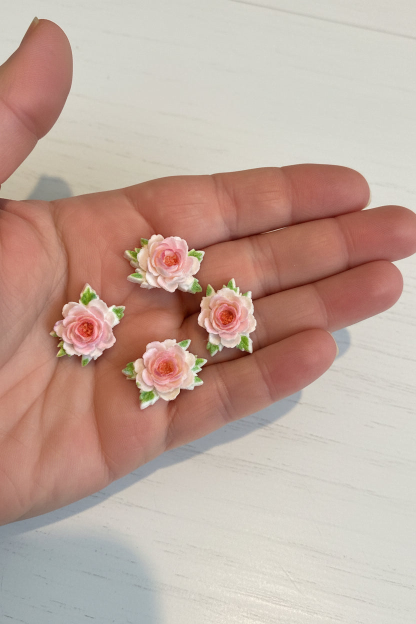 Small soft blue fabric flowers with green leaves held in a hand to show size, craft embellishments pack of 50