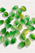 Translucent green glass leaf pendants with golden shimmer and detailed leaf-vein patterns.
