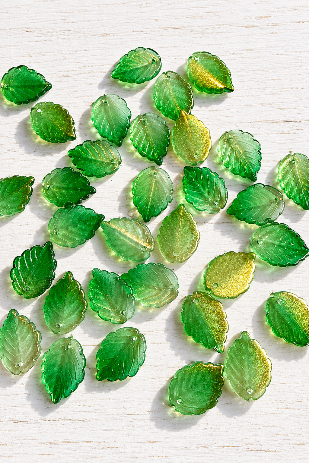 Translucent green glass leaf pendants with golden shimmer and detailed leaf-vein patterns.