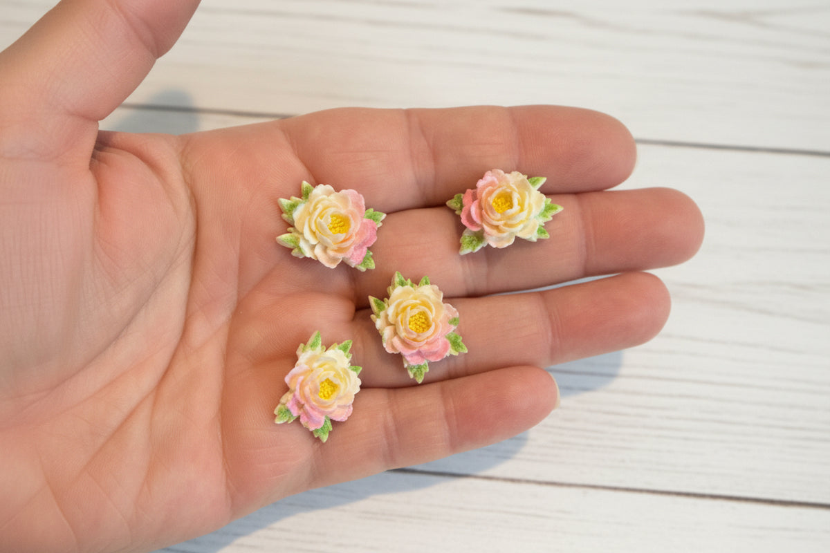 Small soft blue fabric flowers with green leaves held in a hand to show size, craft embellishments pack of 50