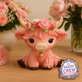 Moo Crew Primrose pink cow figurine with a pink rose crown and gold bell, displayed among pink flowers.